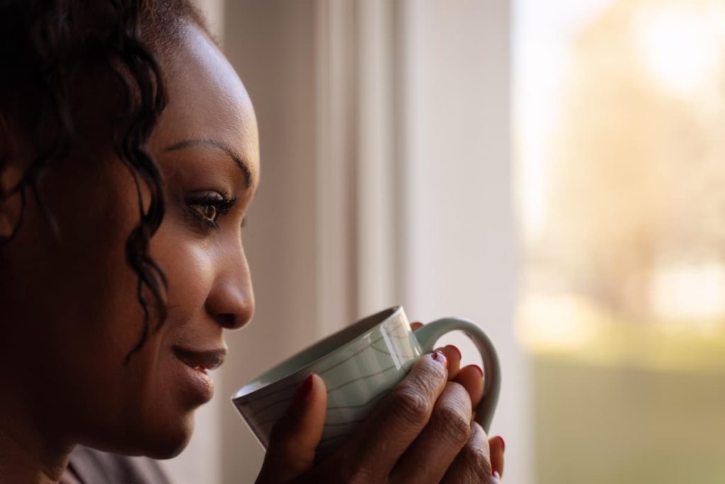 Mujer sosteniendo una taza de té mirando por la ventana, representando la pausa consciente frente al hambre emocional por SOP