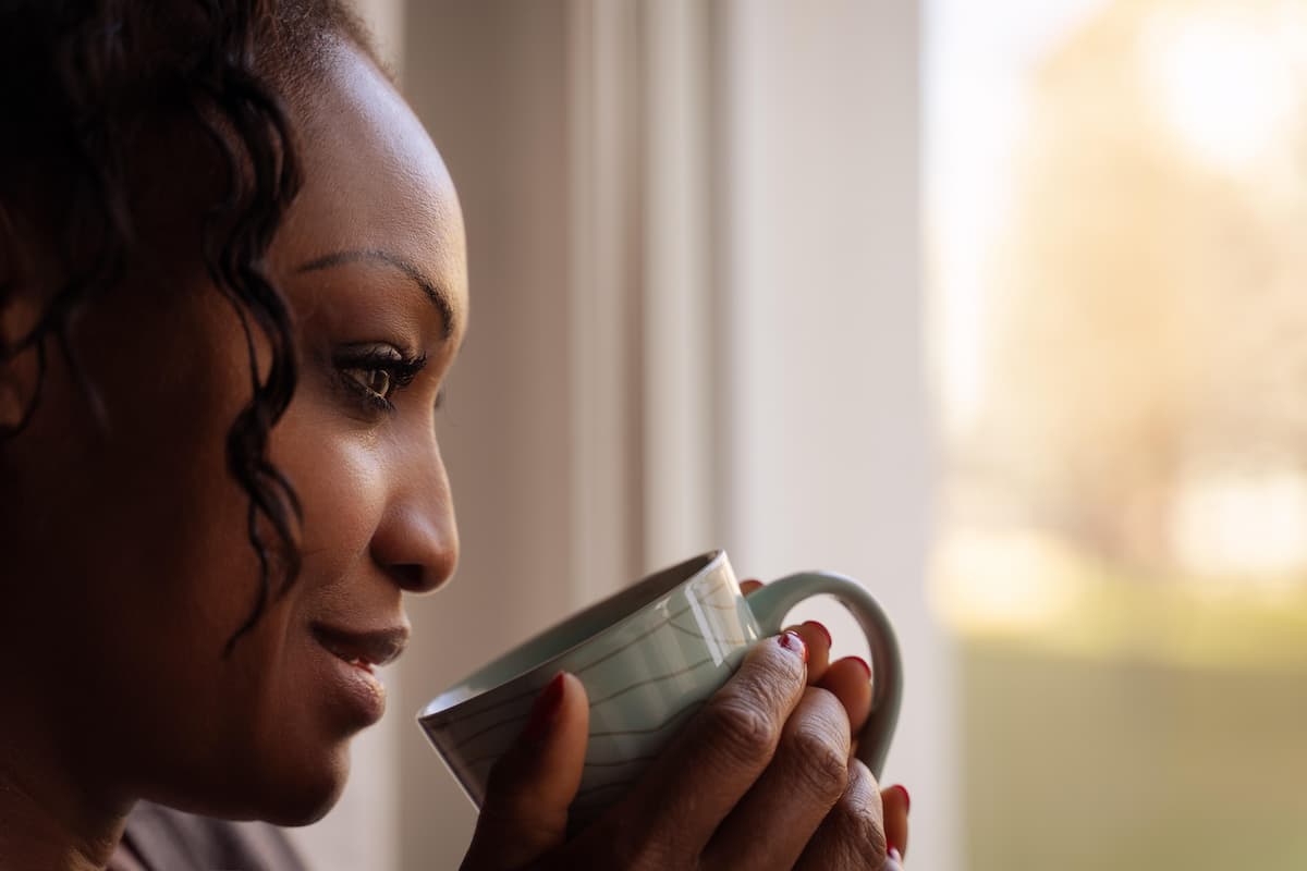 Mujer sosteniendo una taza de té mirando por la ventana, representando la pausa consciente frente al hambre emocional por SOP